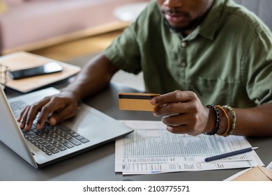 Hands of young man with credit card pressing keys of laptop keypad while sitting by table and shopping online