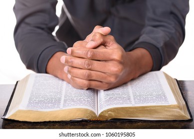 Hands of a young man folded together and praying over a Bible, hands over soft focus Bible.  Bible study and devotion.