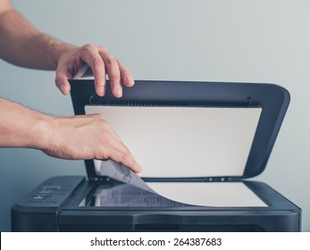 The Hands Of A Young Man Is Placing A Piece Of Paper On A Flatbed Scanner In Preparation For Copying It