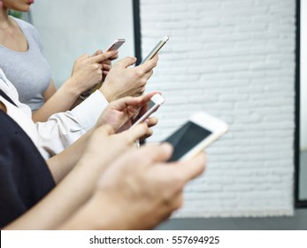 Hands Of Young People Sitting Together Playing With Mobile Phones.