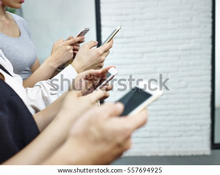 hands of young people sitting together playing with mobile phones.