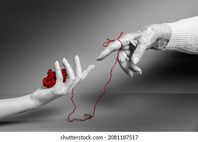 Hands of a young and an senior woman reach out to each other, connected by a red threads. Monochrome. The concept of Alzheimer's and Parkinson's disease.