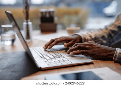 Hands of young solopreneur typing on laptop keyboard in cafe while sitting by table and working with electronic documents