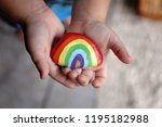 The hands of a young toddler child are gently holding an acrylic painted rainbow rock.