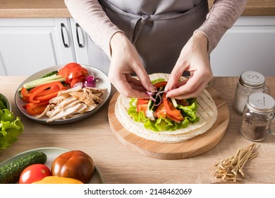 the hands of a young woman carefully lay out pieces of chicken fillet on green lettuce leaves on a grilled flatbread. preparation of buritto at home