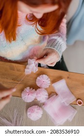 Hands Of A Young Woman In Colorful Handmade Sweater With Scissors Sewing A Ribbon Making DIY Tulle Head Bands At The Table. Close Up. Hobby And Business For Women