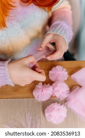 Hands Of A Young Woman In Colorful Handmade Sweater With Scissors Sewing A Ribbon Making DIY Tulle Head Bands At The Table. Close Up. Hobby And Business For Women