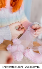 Hands Of A Young Woman In Colorful Handmade Sweater With Scissors Cutting A Ribbon Making DIY Tulle Head Bands. Close Up. Hobby And Business For Women