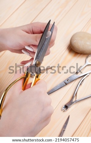 the hands of young woman cutting off long nails with big scissors.