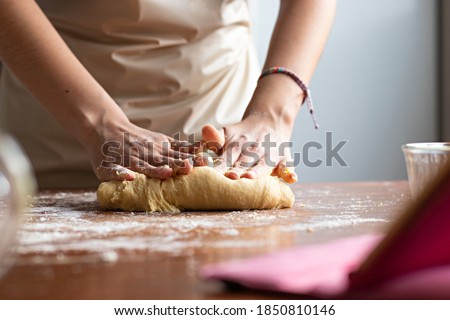 Hands of a young woman, kneading dough to make bread on top of a wooden table