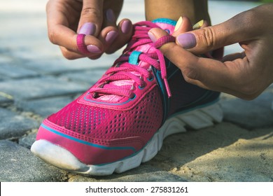 Hands of a young woman lacing bright pink and blue sneakers. Shoes standing on the pavement of stones and sand. In female hands purple-yellow manicure. Photographed close-up. - Powered by Shutterstock