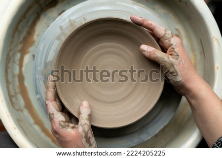 Hands of young woman master of ceramics working on a potter's wheel, making plate of clay in own art studio. Close up, top view