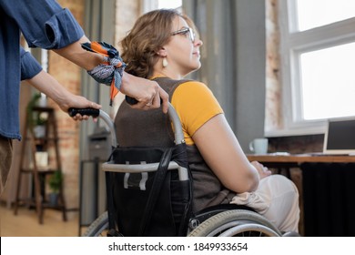 Hands of young woman pushing wheelchair with her disable sister or friend while taking care of her and helping to move around the house