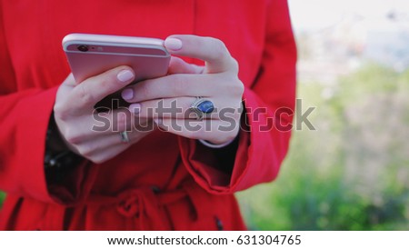 Hands of Young woman in red coat and beautiful ring using her smartphone, Close up