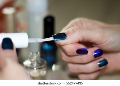 Hands Of A Young Woman Who Is Painting Her Nails A Transparent Top Coat Over Dark Green Metalized Nail Varnish