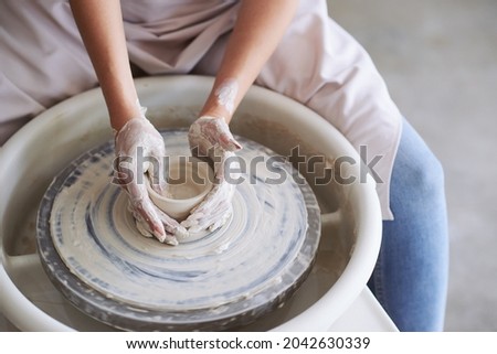 Hands of young woman working on pottery wheel in cozy workshop and making vase or mug