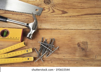 Handsaw, hammer, level, nails and folding ruler on wooden background