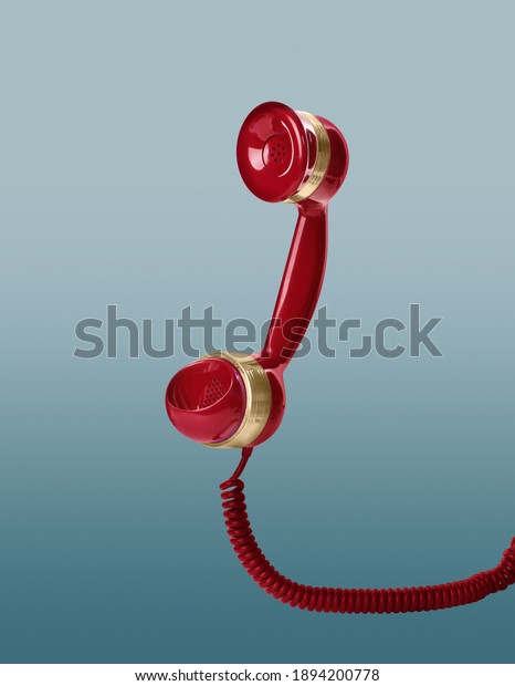 Handset of vintage red corded telephone flying\
in air on light blue\
background