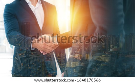 Handshake of 2 businessman in a black suit double exposure the business center city.mergers and acquisitions for start greeting with good etiquette negotiation the success of both