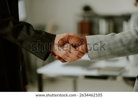Handshake between two professionals in formal business setting, symbolizing agreement and partnership. Office background with blurry objects in scene