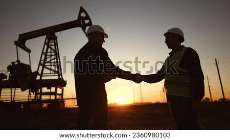handshake business oil contract. handshake worker and businessman shaking hands against sunlight the backdrop of an oil pump. oil extraction business concept. silhouette handshake contract