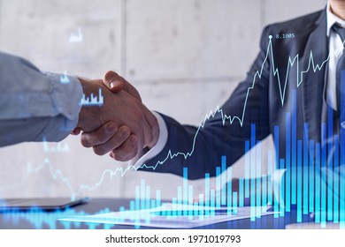 A handshake symbolize a capital market transaction to proceed profitable business in stock trading. Financial hologram chart overt the table with the document. - Shutterstock ID 1971019793