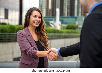 Handshake two business executives downtown buildings man and woman perfect smile teeth hair skin
