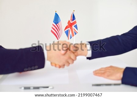 Handshake of two men in front of flags of Great Britain and United States of America symbolize international treaty or business cooperation negotiations between USA and England. Selective focus