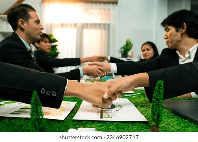 Handshaking between green business partnership over meeting table after made successful corporate solution to solve global warming with implementation of eco-friendly regulation. Quaint