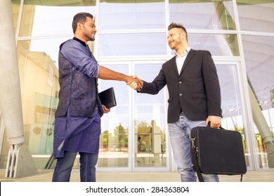 Handshaking Between Two Young Businessmen Holding Laptop - Concept Of Modern Global Market - Outdoor Trade Meeting Between Men Of Different Race And Culture - Happy Students Shaking Hands In The City 