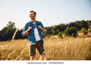 Handsome adult man hiking through meadow with backpack - Powered by Shutterstock