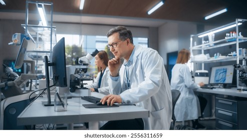 Handsome Adult Scientist Wearing Glasses and a White Lab Coat, Studying DNA Samples and Evaluating Data on Computer. Group of Multiethnic Specialists Working in a Laboratory