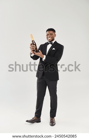 Handsome African American groom in tuxedo holds champagne bottle, poised for celebratory toast.
