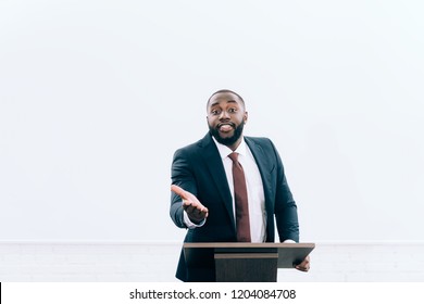 handsome african american lecturer standing at podium tribune and gesturing during seminar in conference hall - Powered by Shutterstock