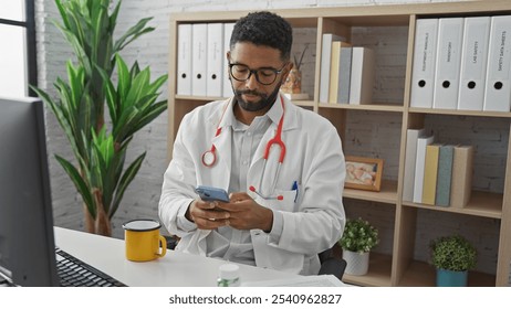 A handsome african american male doctor in a white coat with a stethoscope, checking his phone in a modern clinic office. - Powered by Shutterstock