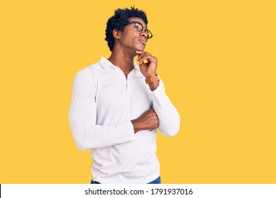 Handsome african american man with afro hair wearing casual clothes and glasses with hand on chin thinking about question, pensive expression. smiling with thoughtful face. doubt concept. 