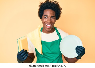 Handsome African American Man With Afro Hair Wearing Apron Holding Scourer Washing Dishes Smiling And Laughing Hard Out Loud Because Funny Crazy Joke. 