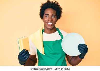 Handsome African American Man With Afro Hair Wearing Apron Holding Scourer Washing Dishes Smiling With A Happy And Cool Smile On Face. Showing Teeth. 