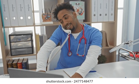 Handsome african american man with a beard working in a veterinary clinic, wearing scrubs and a stethoscope, multitasking with a phone and computer in a bright, organized interior. - Powered by Shutterstock