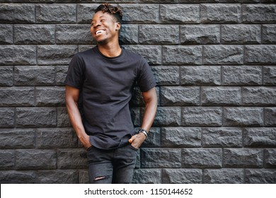 Handsome african american man in black t-shirt laughing against brick wall - Powered by Shutterstock