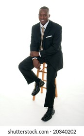 Handsome African American Man In A Black Business Suit Casually Sitting On A Stool.