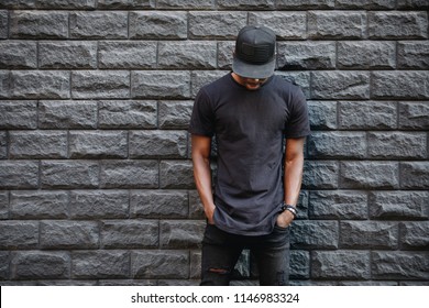 Handsome african american man in blank black t-shirt standing against brick wall