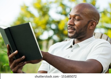 Handsome African American Man In His Late 20s Reading A Book At The Park On A Summer Day