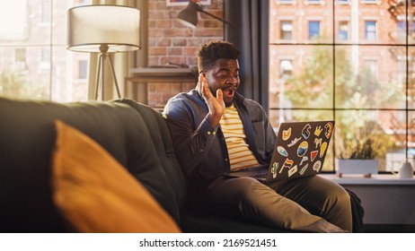 Handsome African American Man Making a Video Call on Laptop Computer in Sunny Stylish Loft Apartment. Creative Person Talking with Friends, Colleagues or Family. Urban City View from Big Window.