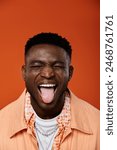 Handsome African American man playfully sticks out his tongue against a vibrant orange backdrop.