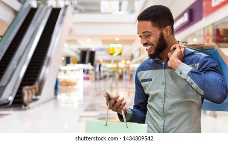 Handsome african american man with shopping bags using cellphone and smiling in mall center, panorama, copy space