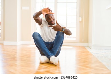 Handsome african american man sitting on the floor at home smiling making frame with hands and fingers with happy face. Creativity and photography concept. - Shutterstock ID 1369898420