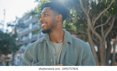 A handsome african american man smiles in a sunny urban setting with trees and buildings in the background. - Powered by Shutterstock