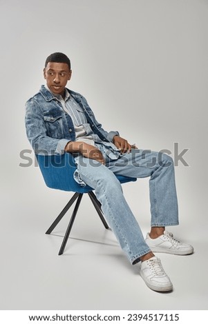 handsome african american man in stylish denim outfit sitting on blue chair, fashion concept