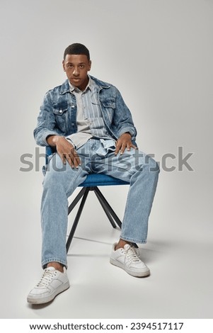 handsome african american man in stylish denim outfit sitting on blue chair, fashion concept
